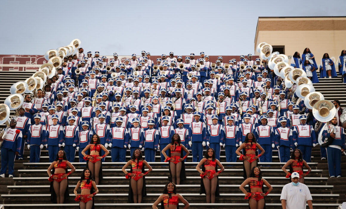 The Tennessee State University Marching Band sitting in the stands of their stadium. The color guard is in the foreground, with the band in the back.