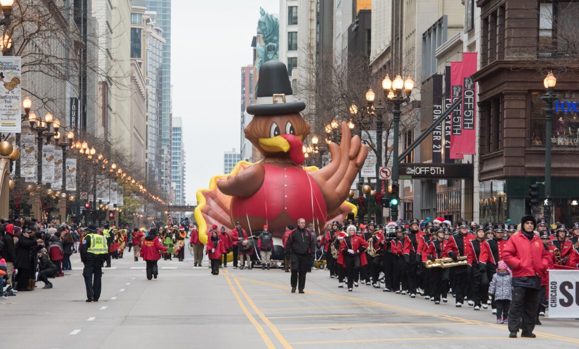 The Marist High School Marching Band, followed by the Teddy Turkey cold-air inflatable balloon, march down State Street during the Chicago Thanksgiving Parade.