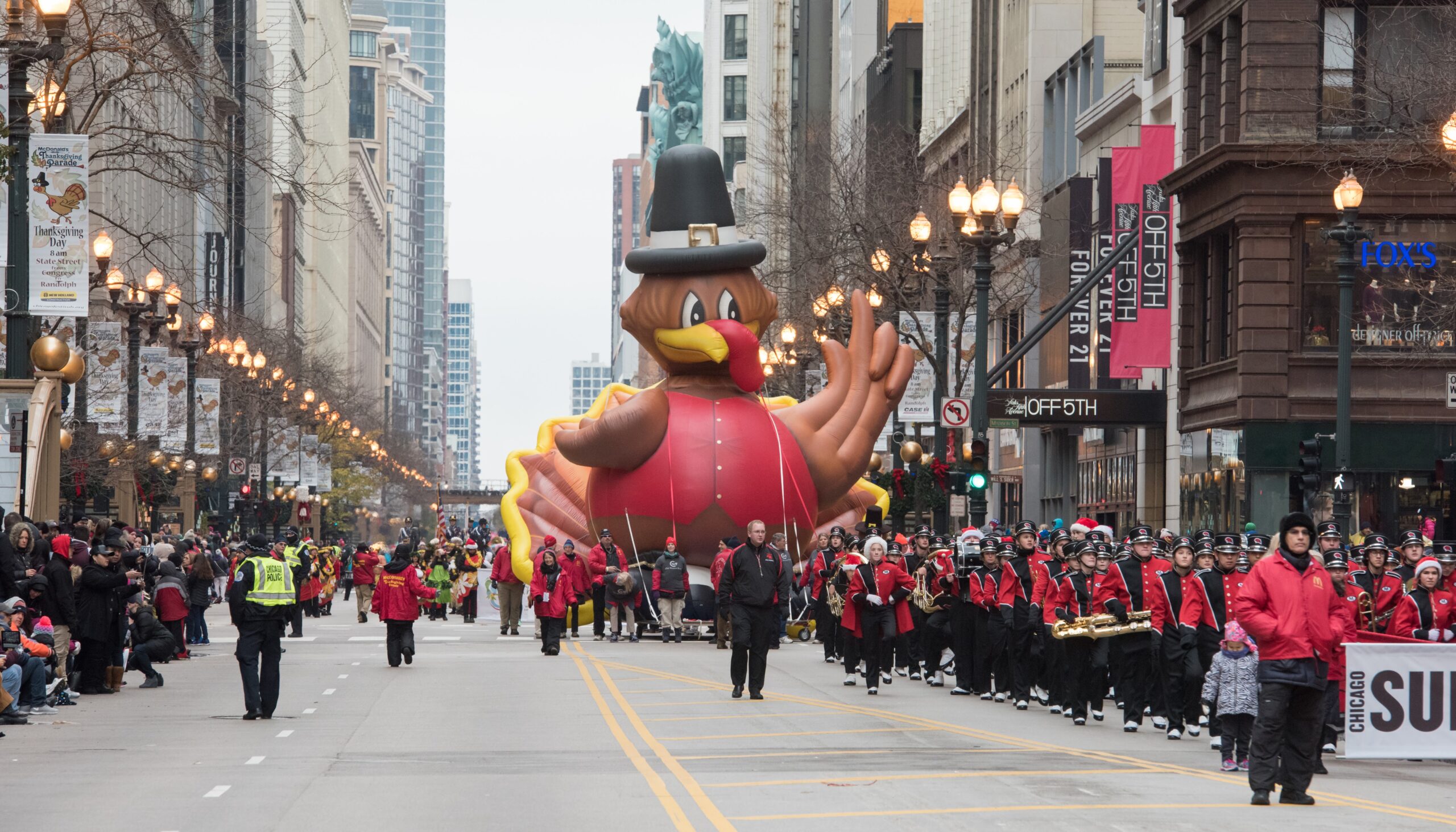 2016 Teddy Turkey Balloon (8) The Marist High School Marching Band, followed by the Teddy Turkey cold-air inflatable balloon, march down State Street during the Chicago Thanksgiving Parade.